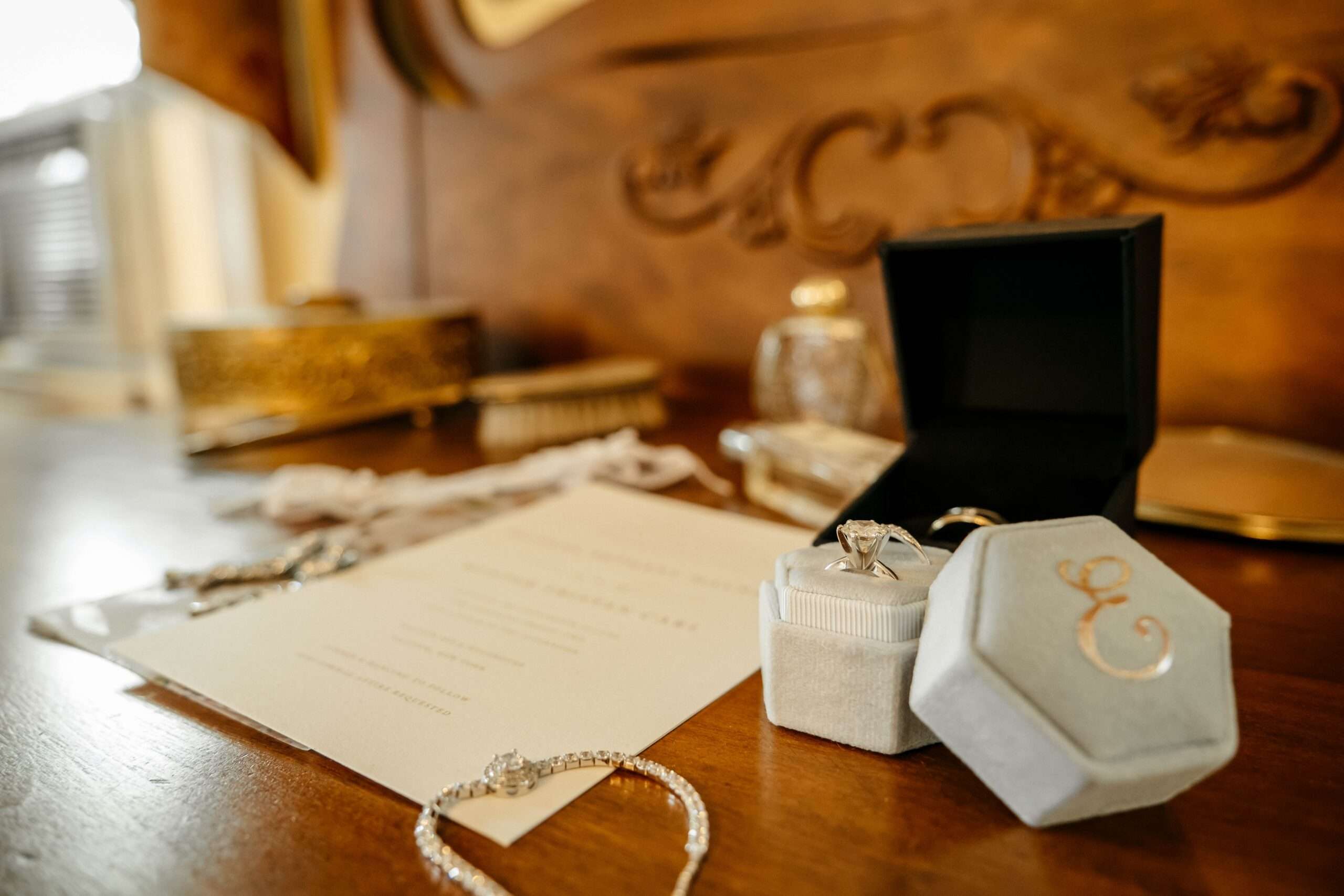 Engagement ring in a velvet box beside a bracelet and stationery on a wooden vanity