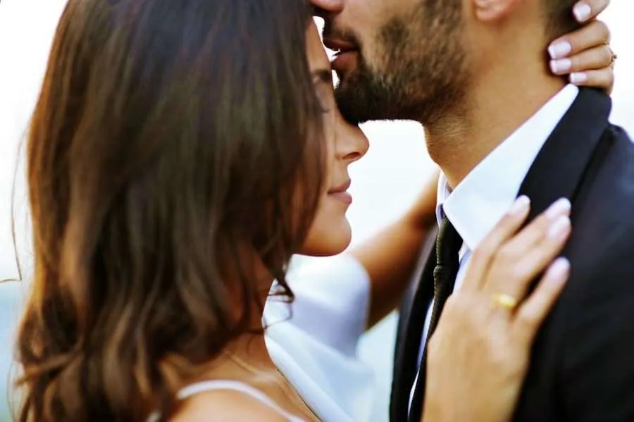 Groom kissing his bride's forehead in a close-up embrace