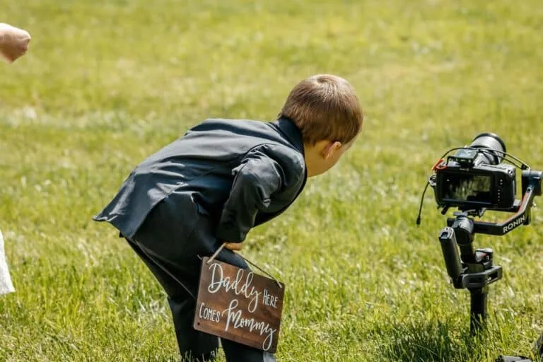Ring bearer with "Daddy here comes Mommy" sign filmed by the best wedding photographer in New England during outdoor ceremony | Love in Focus Studio