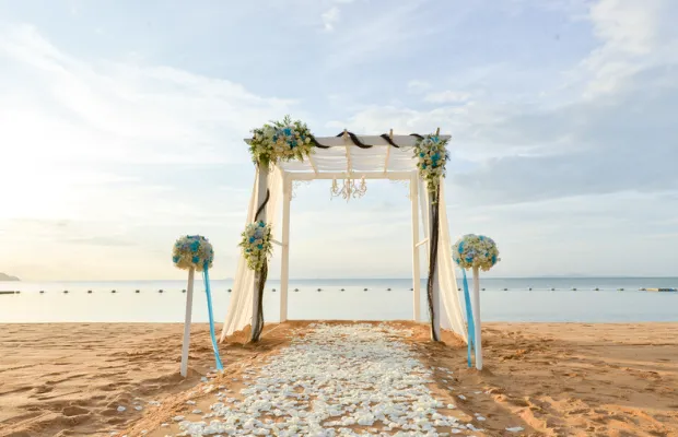Beach wedding canopy with blue flowers and a petal-lined aisle by the ocean