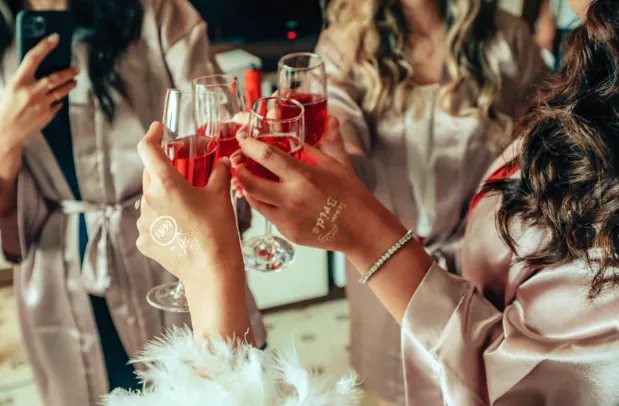 Bridesmaids in satin robes toasting with drinks while getting ready