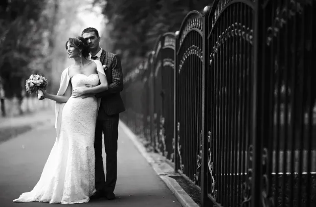 Black-and-white portrait of a couple beside a wrought-iron fence