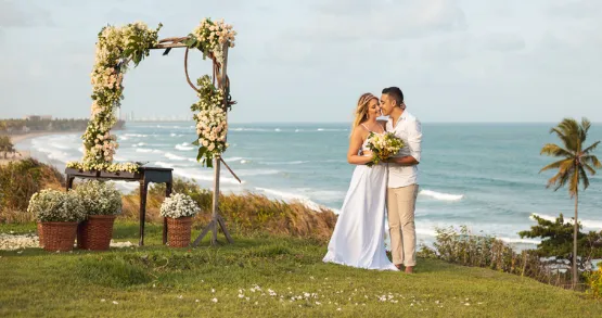 Couple embracing beneath a floral arch at a clifftop ceremony overlooking the sea