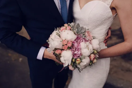 Close-up of a pastel bouquet of peonies and roses held between a couple