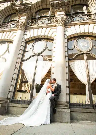 A bride and groom kiss outside The Dorrance in Providence, Rhode Island, a grand building with ornate windows and columns.