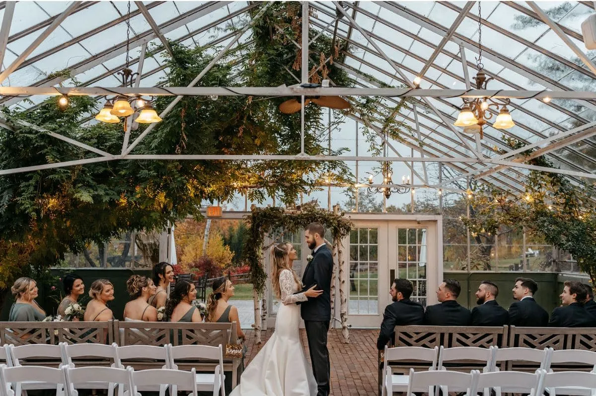 A bride and groom stand at the altar during their wedding ceremony inside the greenhouse at The Barn on the Pemi in Plymouth, New Hampshire.