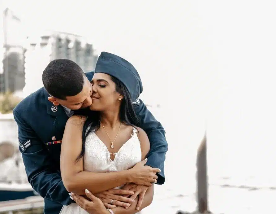 A groom in a military uniform kisses his bride's cheek during their wedding at the Boston Harbor Hotel.