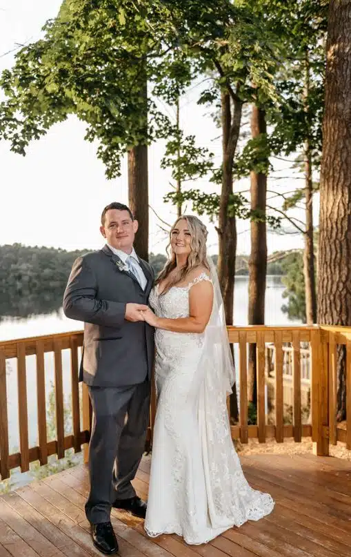 A bride and groom hold hands while posing on a lakeside deck at Camp Kiwanee in Hanson, Massachusetts.