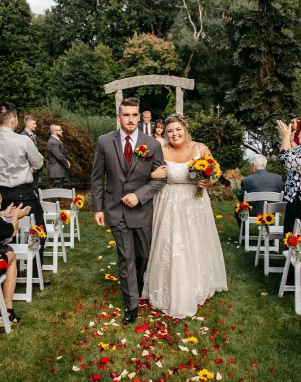 A bride and groom walk down the aisle, covered in petals, after their outdoor ceremony at the Fairfield Inn in Milford, MA.