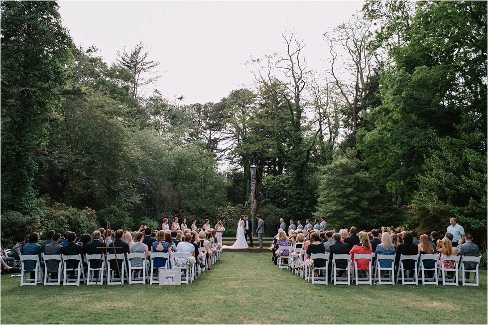 An outdoor wedding at Heritage Museums & Gardens in Sandwich, MA, with guests seated on a lawn surrounded by lush trees.