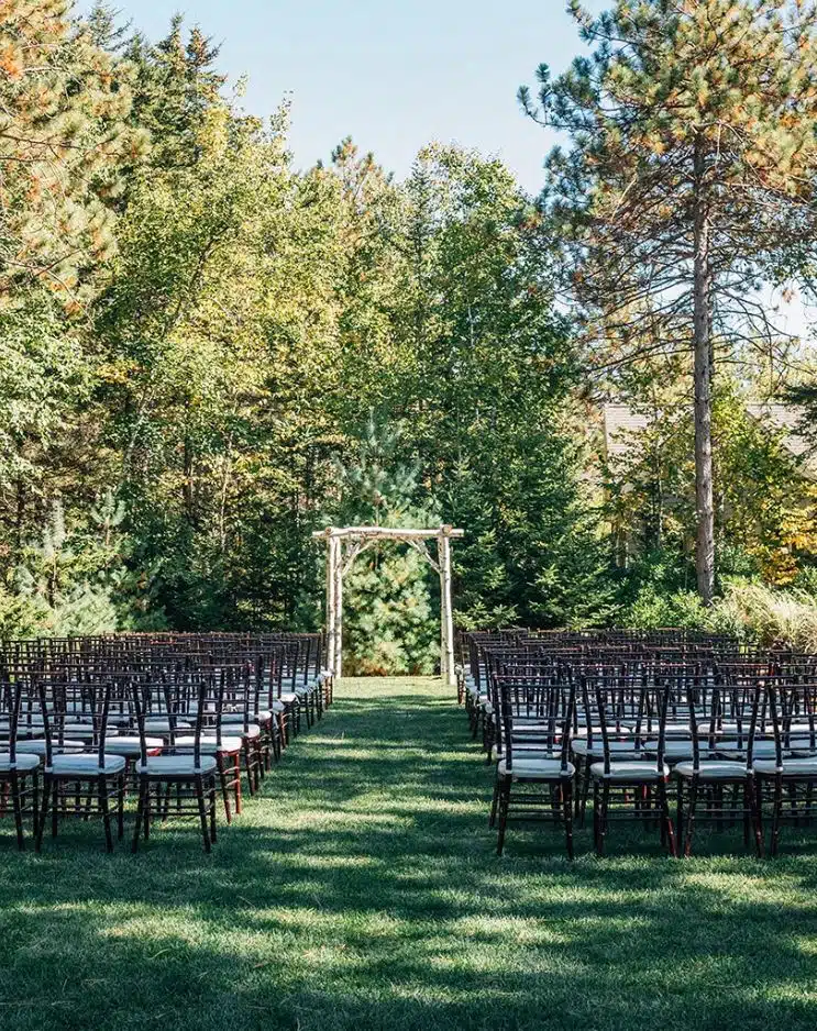 An outdoor wedding ceremony setup at Hidden Pond in Kennebunkport, Maine, with a birch arch at the end of the aisle.