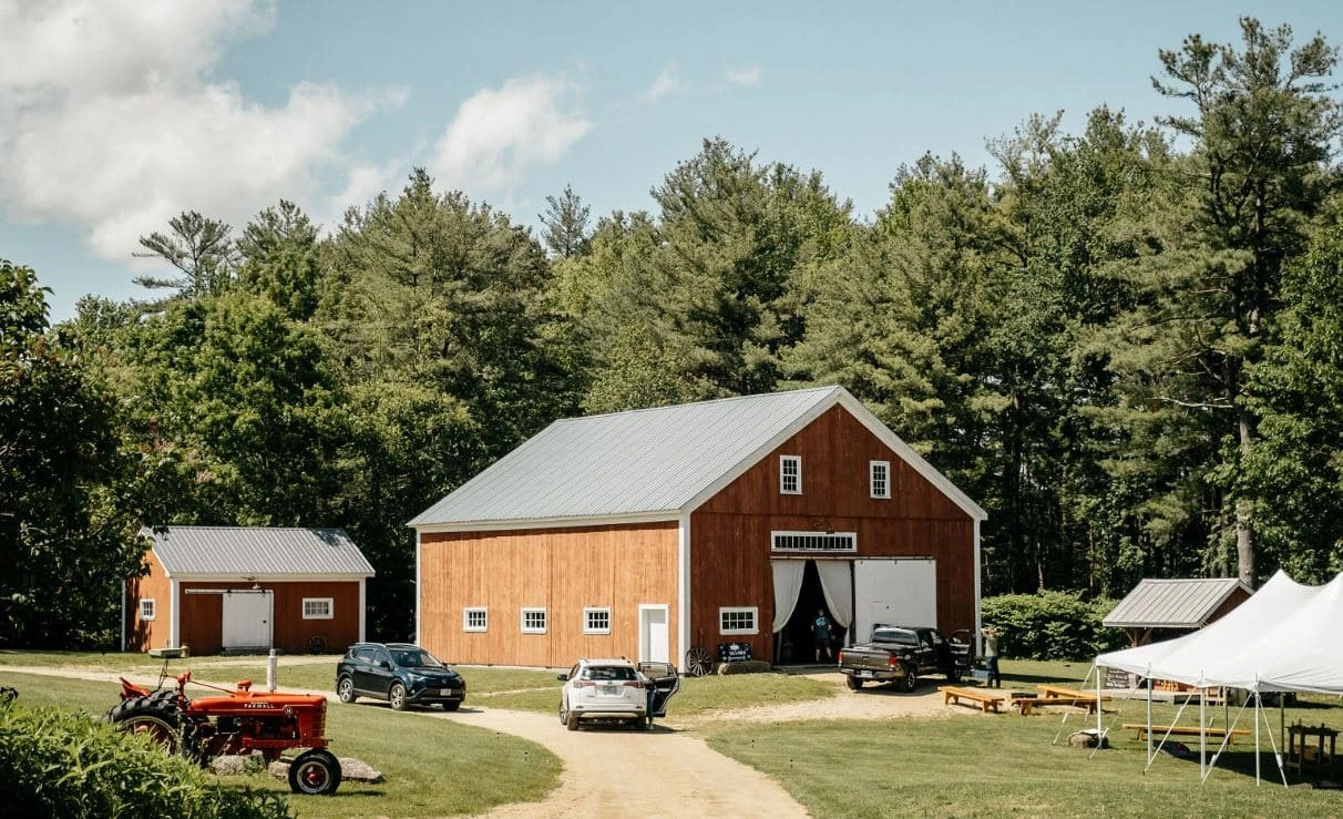 The red wedding barn at Kitz Farm in Strafford, New Hampshire, with a vintage tractor and event tent on a sunny day.