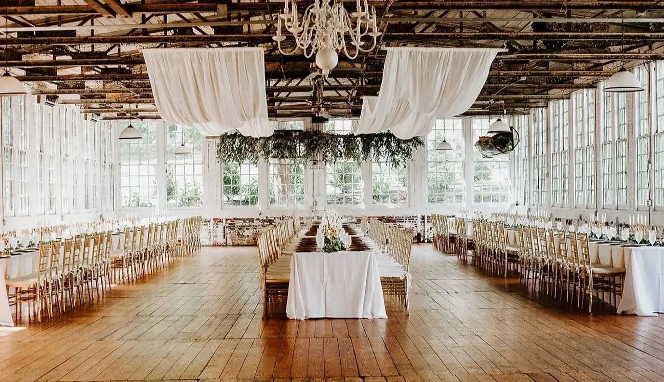 Of course! Here is the alt text for the image you provided: A wedding reception at The Lace Factory in Deep River, CT, with long tables, industrial ceilings, and large windows.