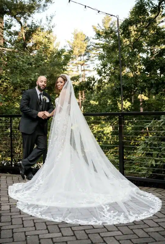 A bride and groom pose on the patio at Lakeview Pavilion in Foxborough, near Boston, with the bride's long veil spread out.