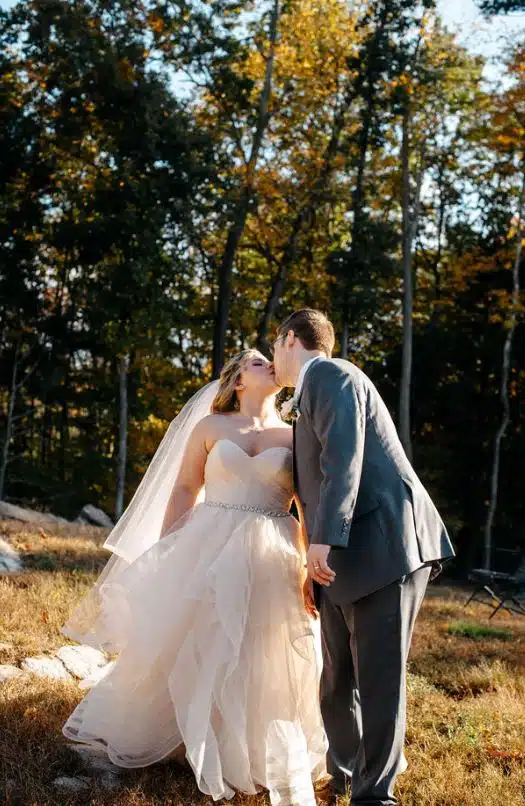 A bride and groom kiss in a sunlit field at Laurel Ridge Bed and Breakfast in Warren, MA, during their autumn wedding.