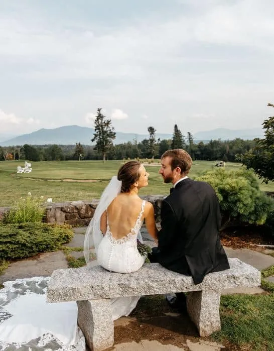 A bride and groom sit on a stone bench overlooking the mountains at Mountain View Grand Resort in Whitefield, New Hampshire.