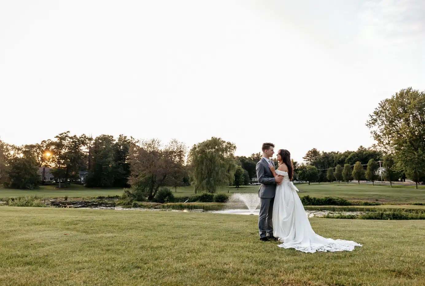 A bride and groom stand on the lawn at Nabnasset Lake Country Club in Westford, MA, with a fountain in the background.