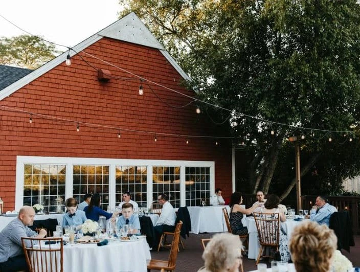 An outdoor wedding reception at The Coonamesset in Falmouth, MA, with guests seated at tables under string lights.