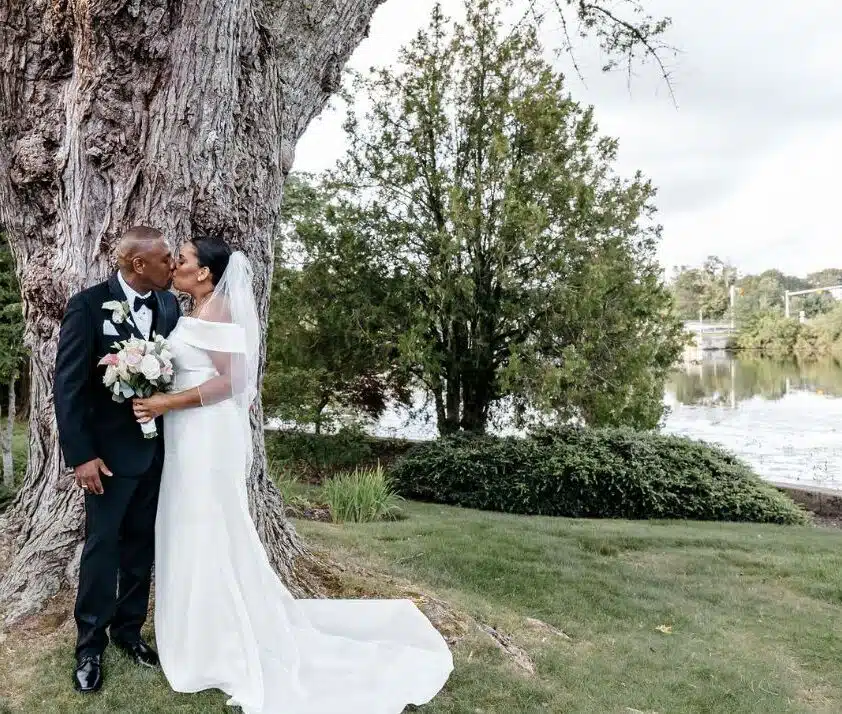 A bride and groom kiss under a large tree by the water during their wedding at Rachel's Lakeside in Dartmouth, Massachusetts.