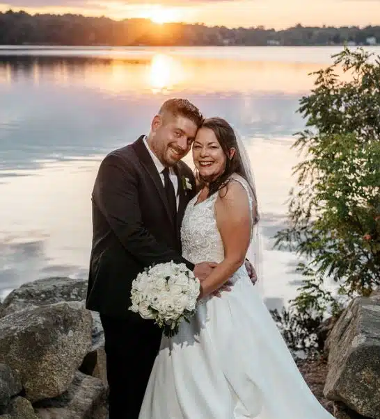 A bride and groom pose by the water at sunset during their wedding at Sapphire Estate in Sharon, Massachusetts.