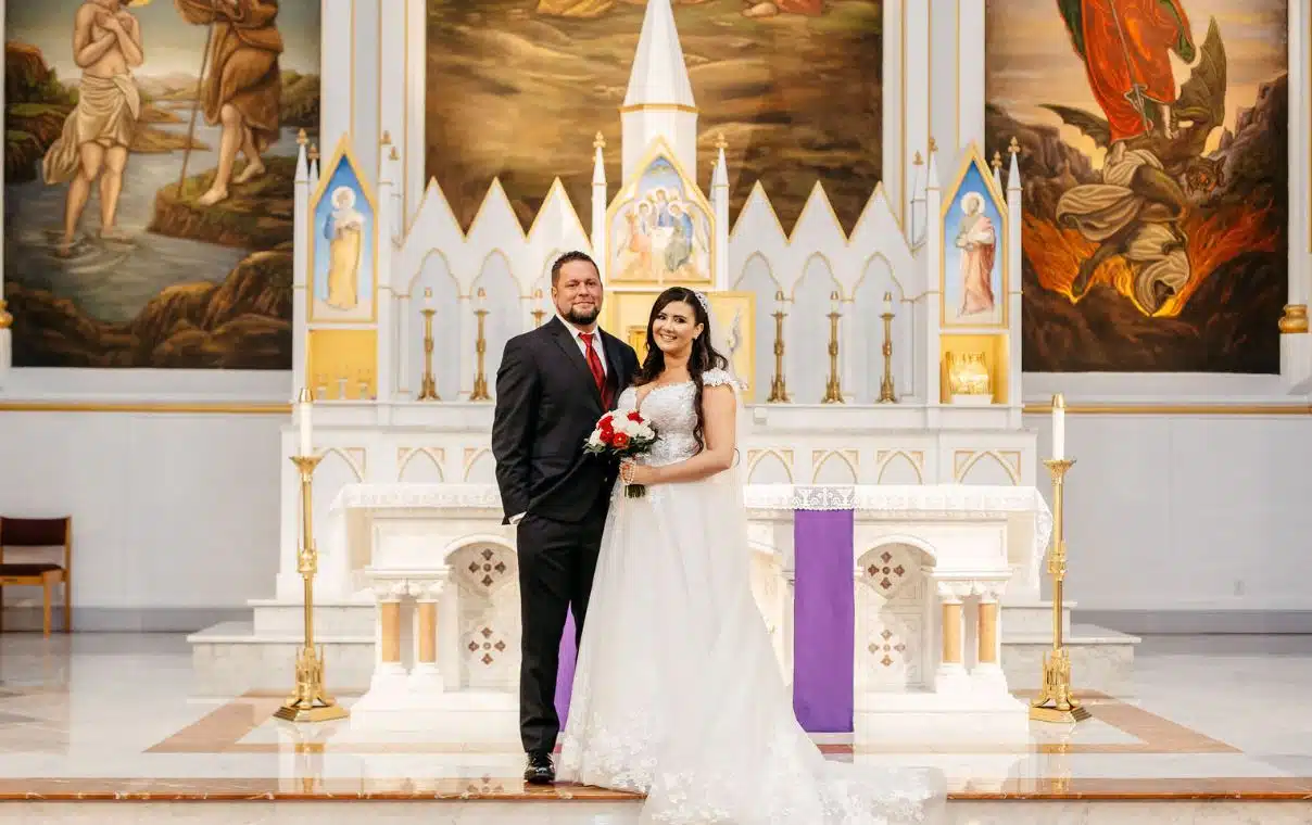 A bride and groom pose for a photo in front of the altar at St. John the Baptist Church in Boston, Massachusetts.