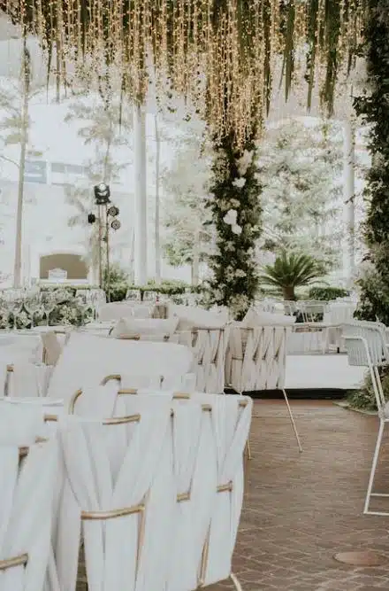 An elegant wedding setup at The Cape Club in East Falmouth, MA, with hanging lights, floral decor, and white chairs.