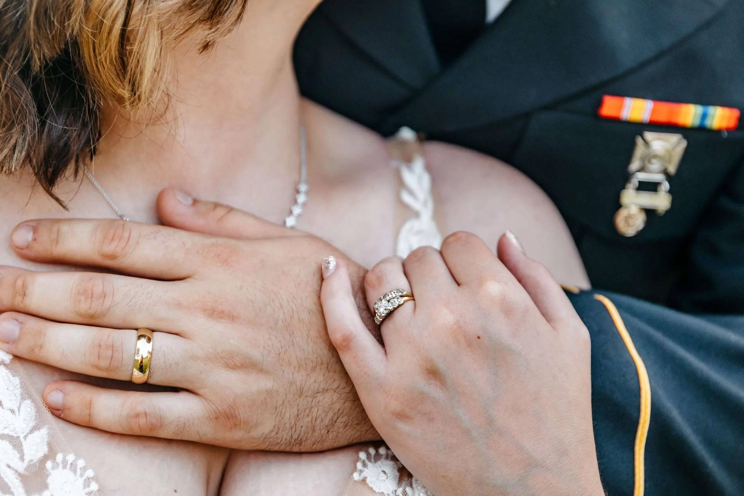 Close-up of newlyweds' hands and rings against an Army dress uniform