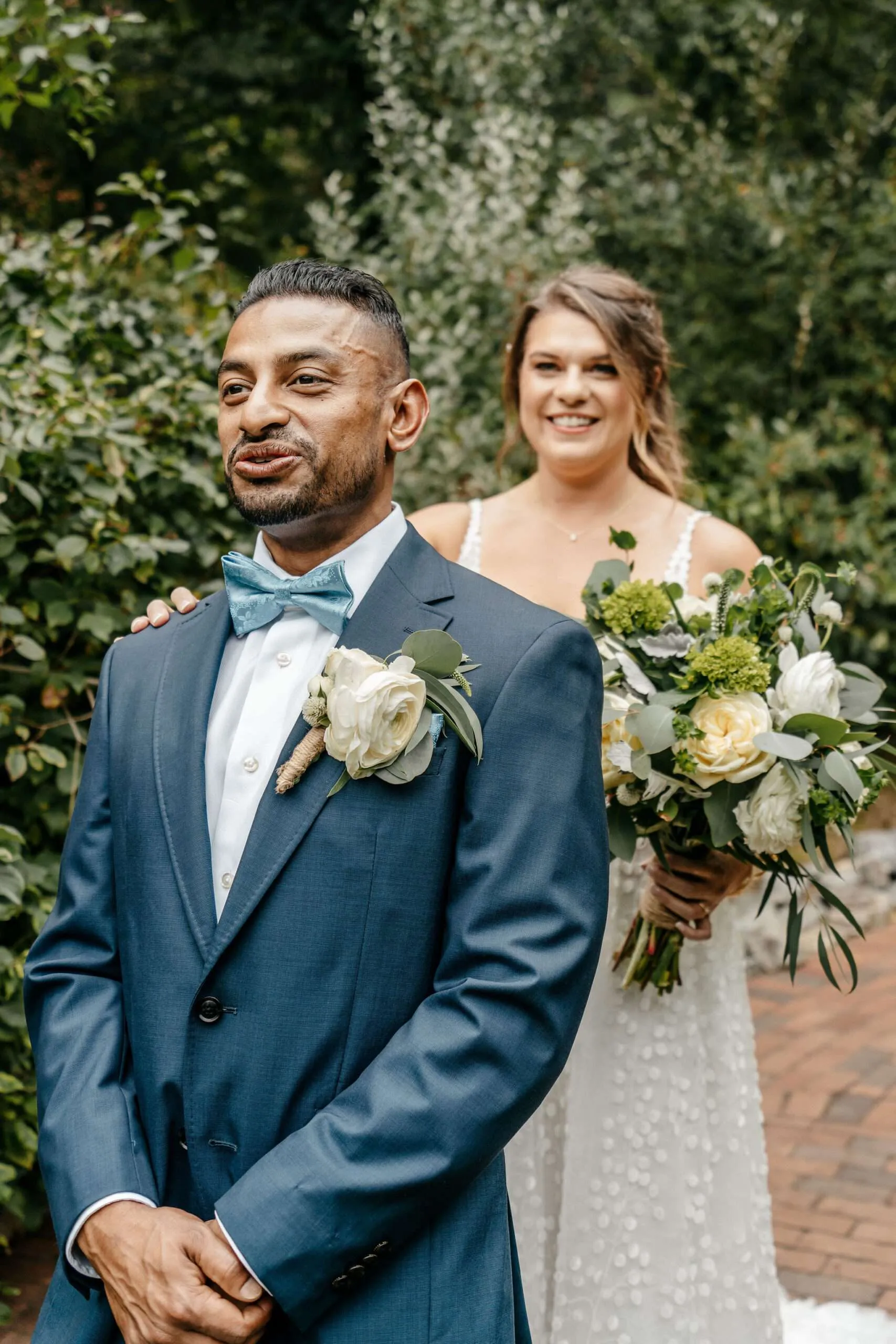 Bride surprising her groom from behind during their first look, bouquet in hand