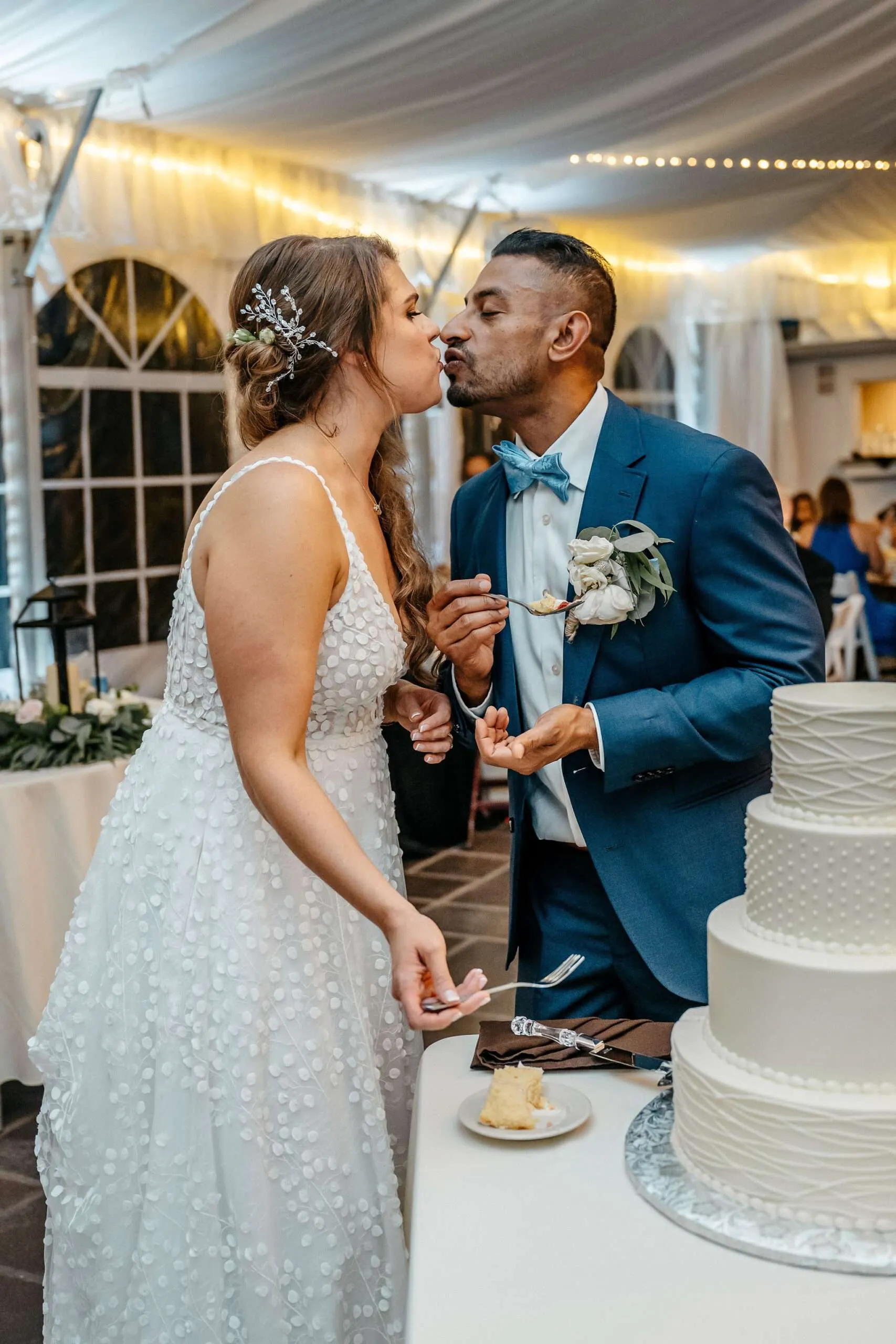 Bride and groom kissing beside their three-tier cake at a tented reception