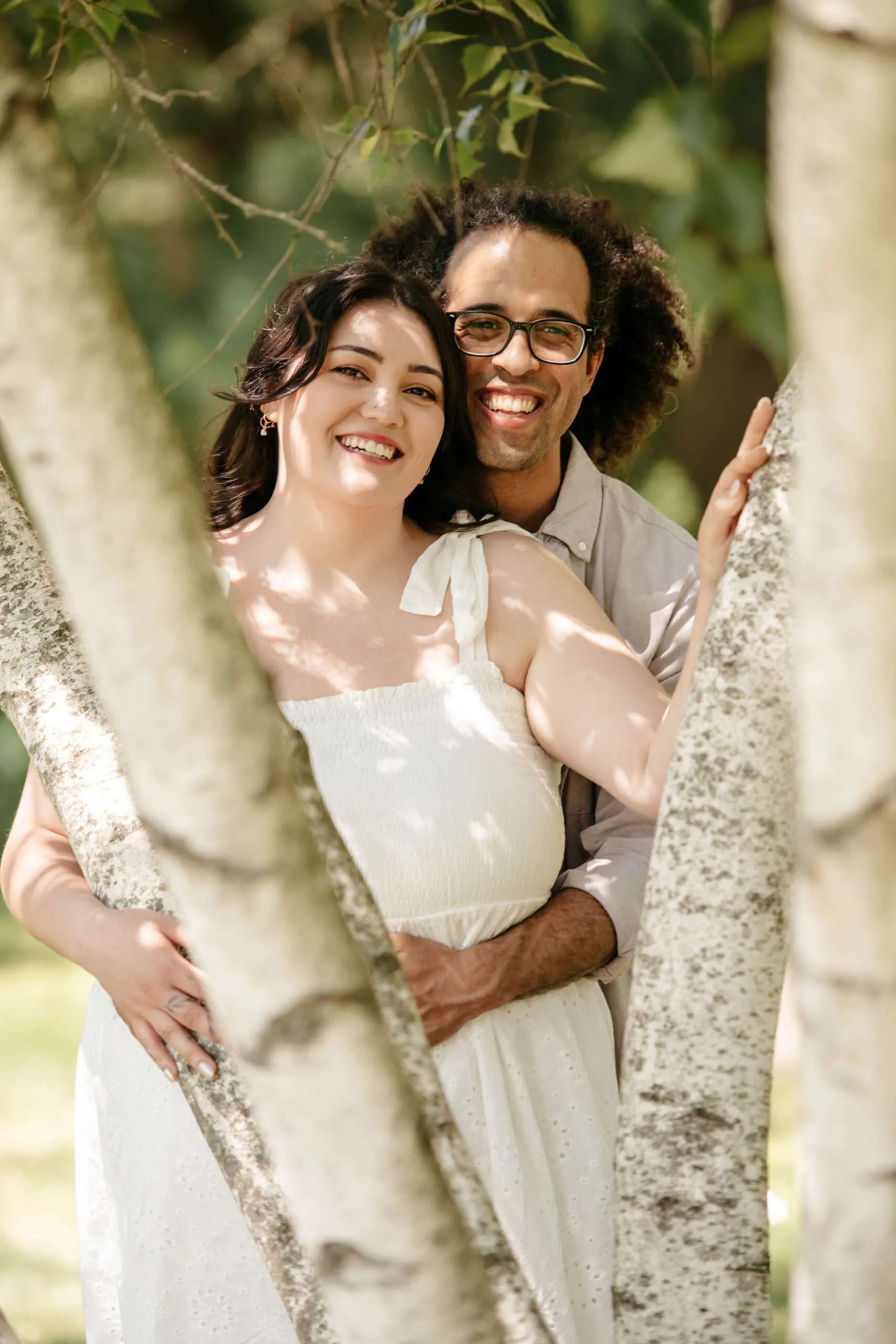 Couple embracing behind tree trunks.