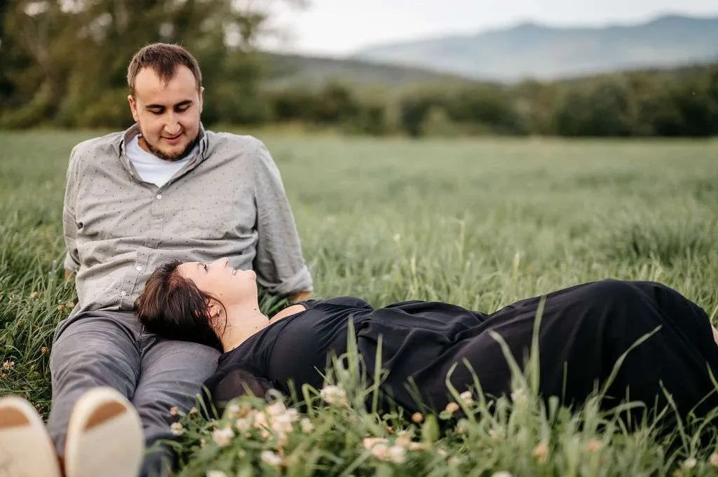 Brady sitting on the grass with his Monique's head on his lap during their pre-wedding engagement session in Gorham New Hampshire.