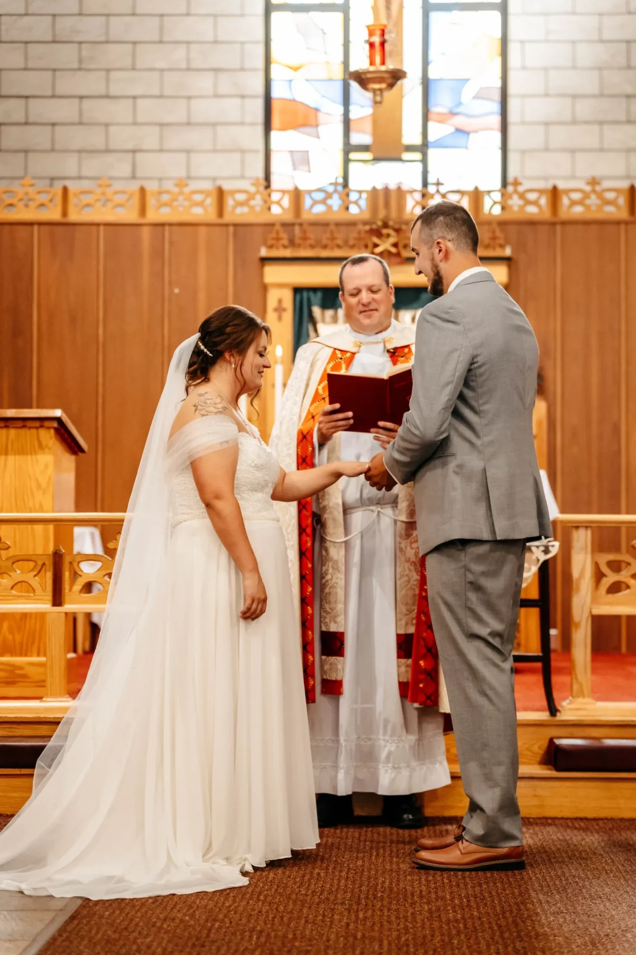 Bride and groom holding hands before the priest during the ceremony at Holy Family Roman Catholic Church in Gorham, NH.