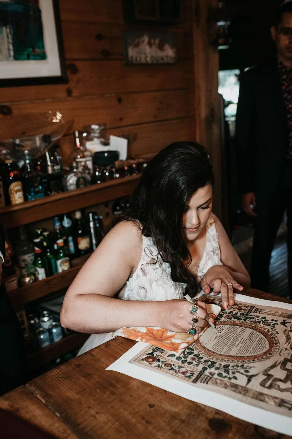A bride signs her Ketubah, the Jewish marriage contract, at a wooden table at Moose Pond Cabin in Townshend, Vermont.