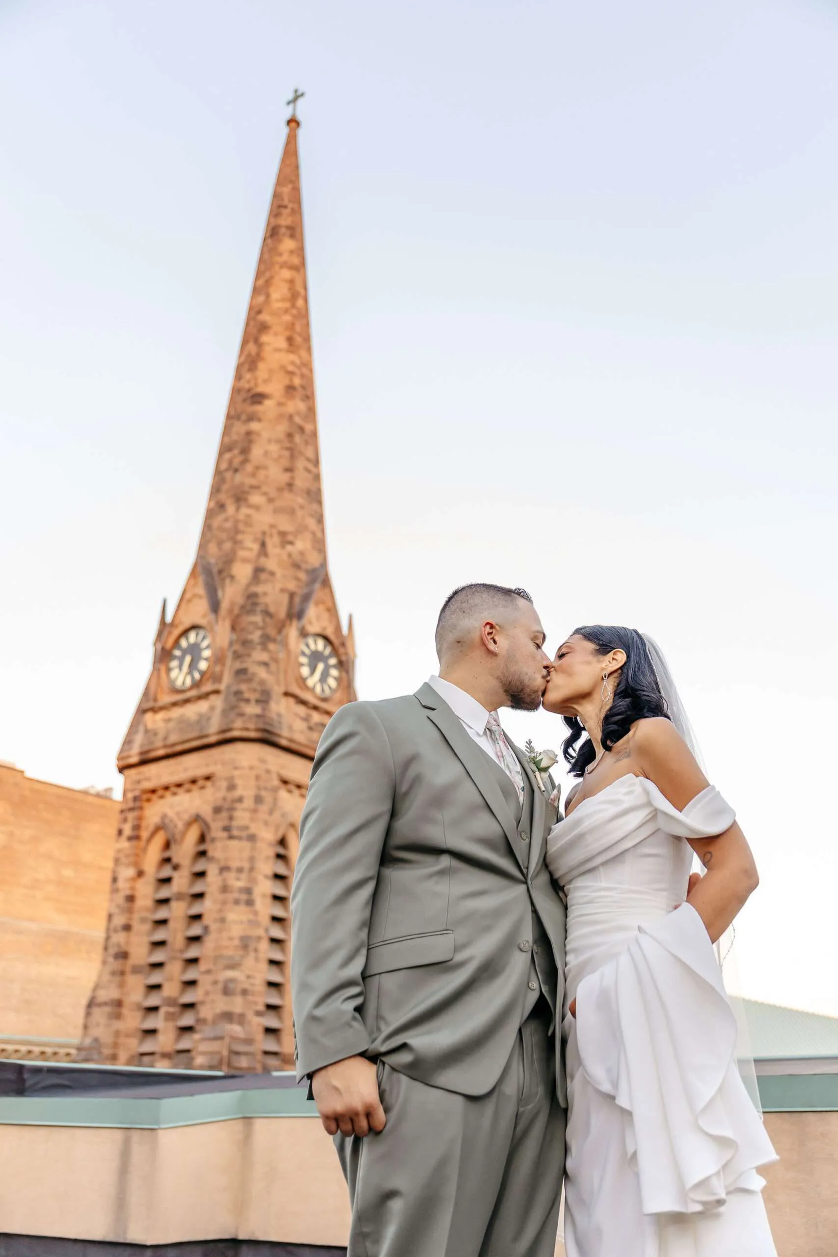 Couple kissing near church steeple.