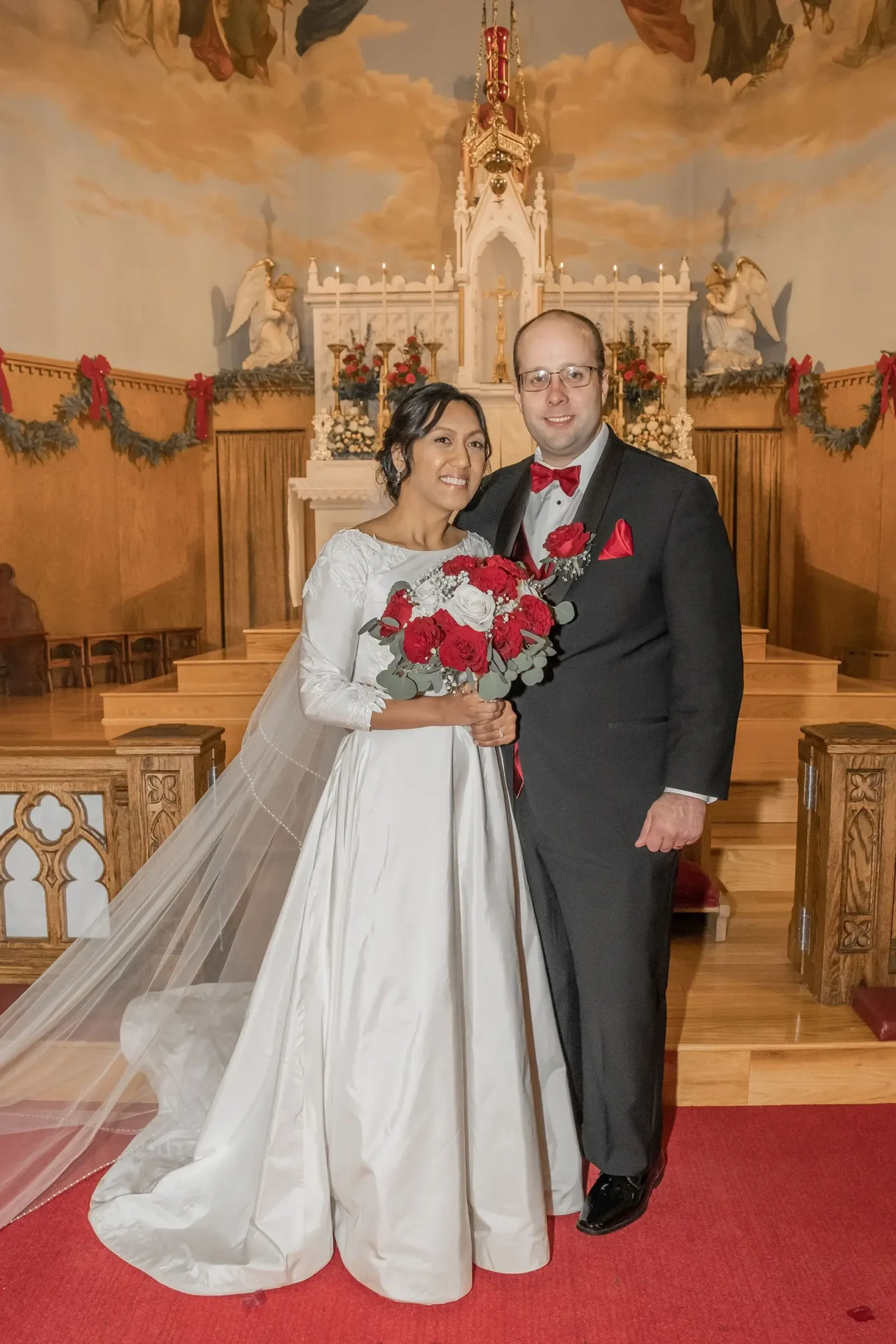 Bride and groom posing at the altar decorated with red poinsettias at St. Stanislaus Catholic Church in Nashua, NH.