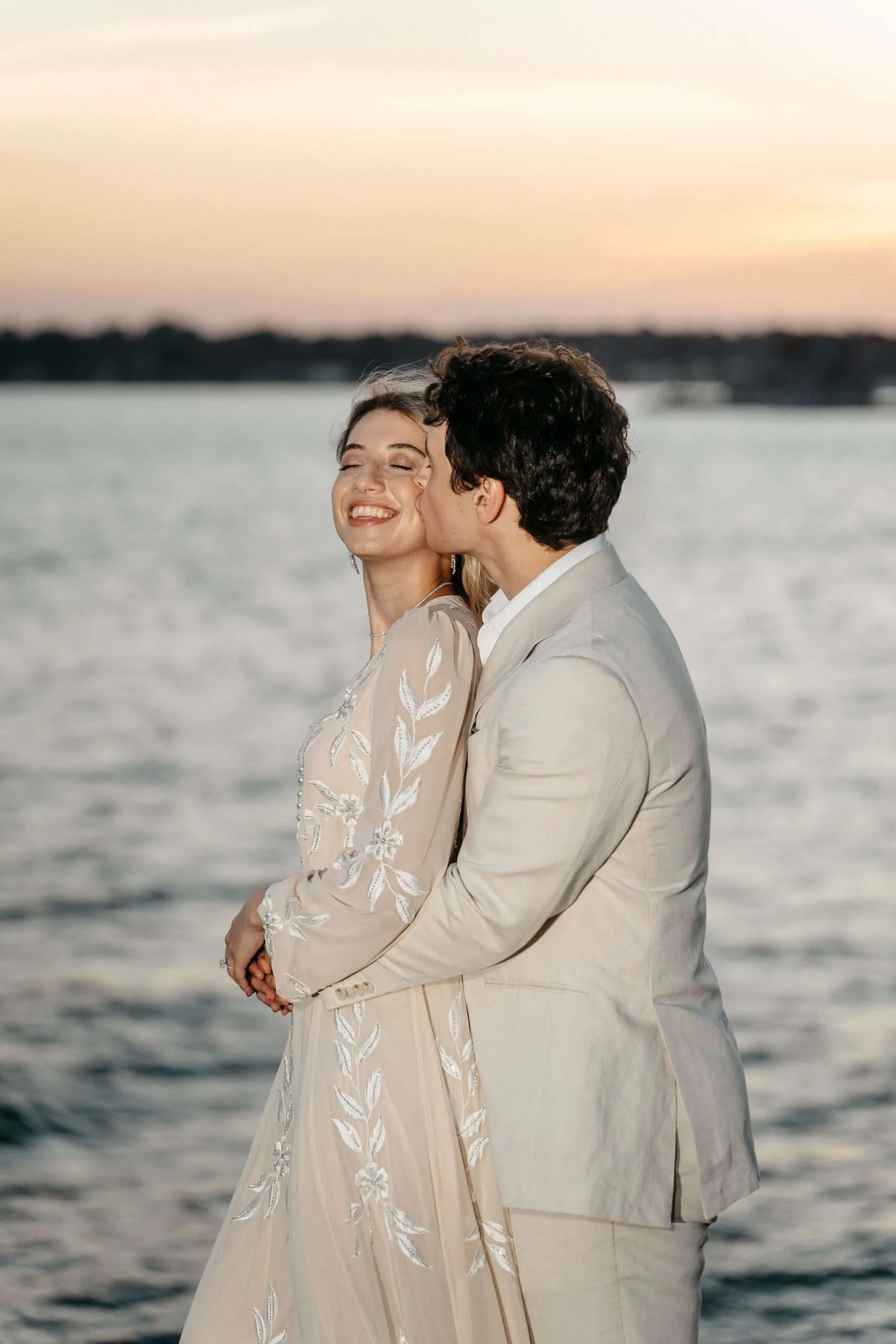 Groom kissing bride on the cheek at sunset on the shoreline at the Branford House in CT>