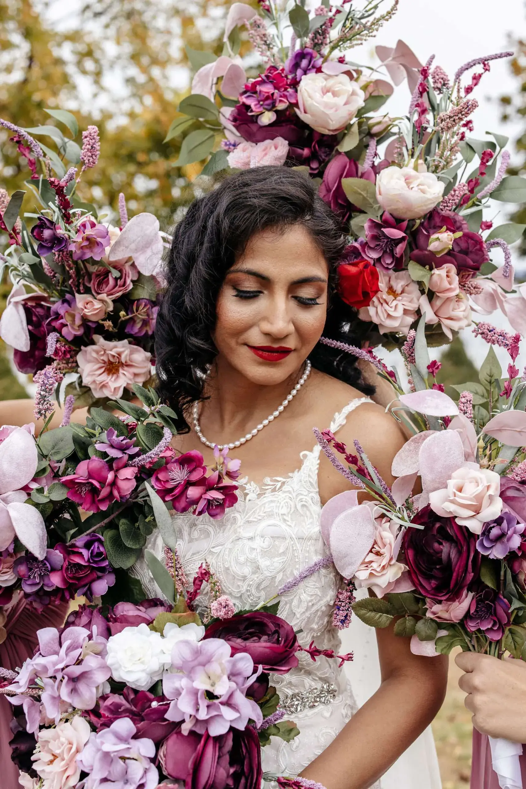 A beautiful bride is surrounded by her bridesmaids' bouquets of purple and pink flowers at Valcour Inn & Boathouse in Peru, NY.