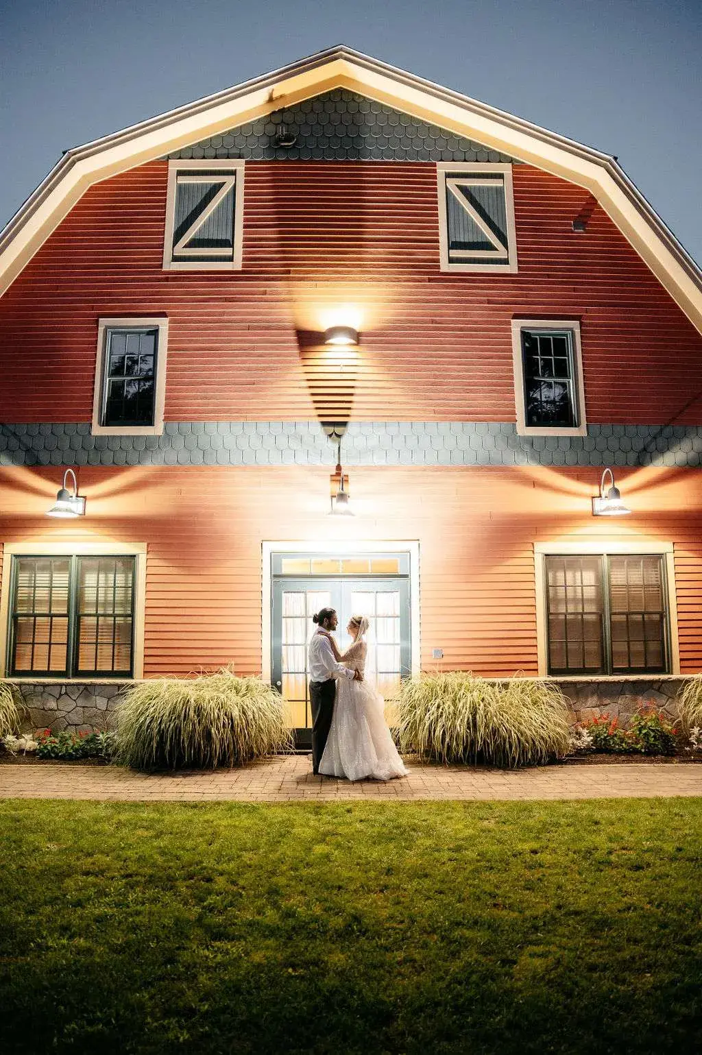 A bride and groom pose for a nighttime photo in front of the red barn at the Wyndham Newport Hotel in Middletown, RI.