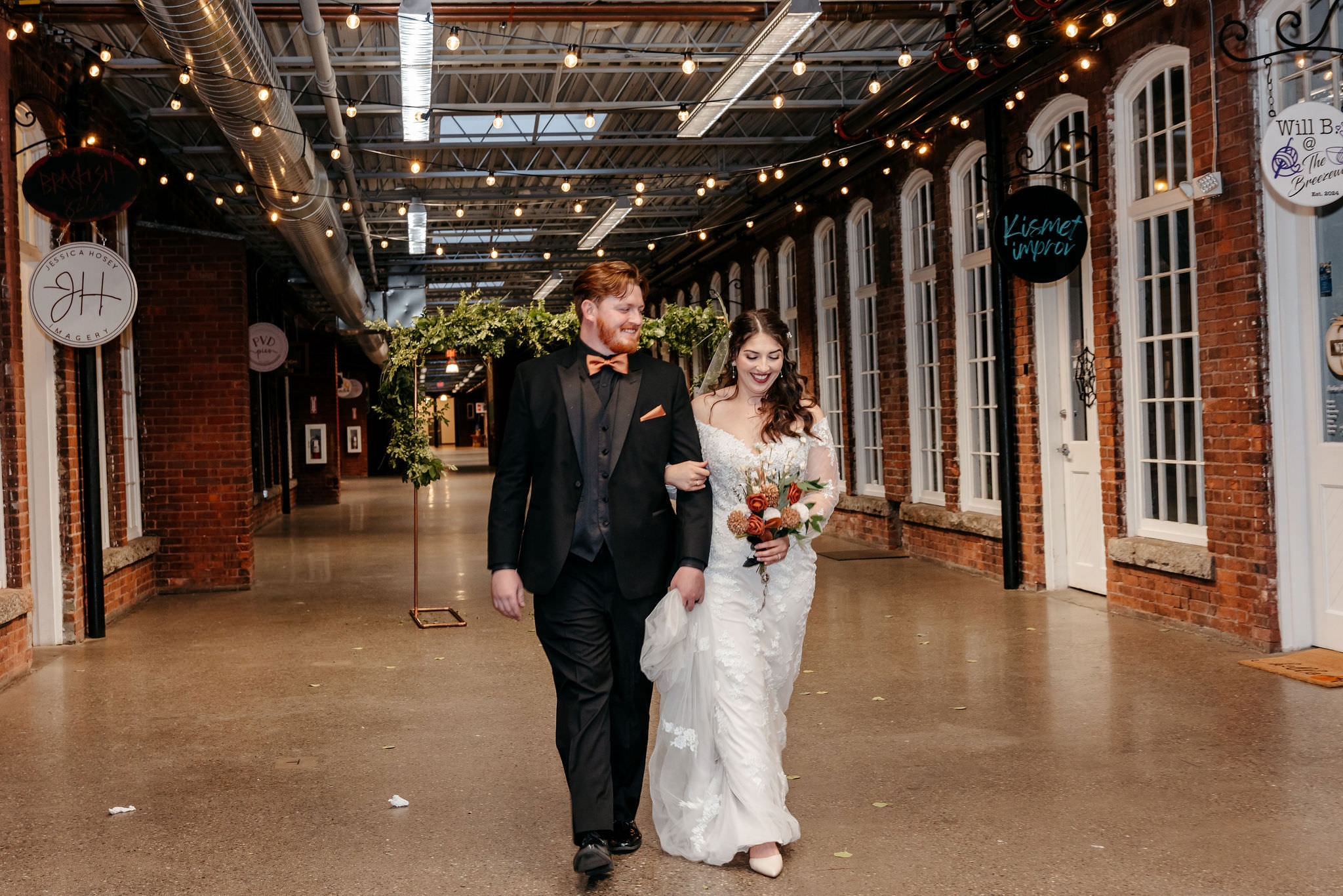 Newlyweds walking arm in arm through a string-lit brick breezeway