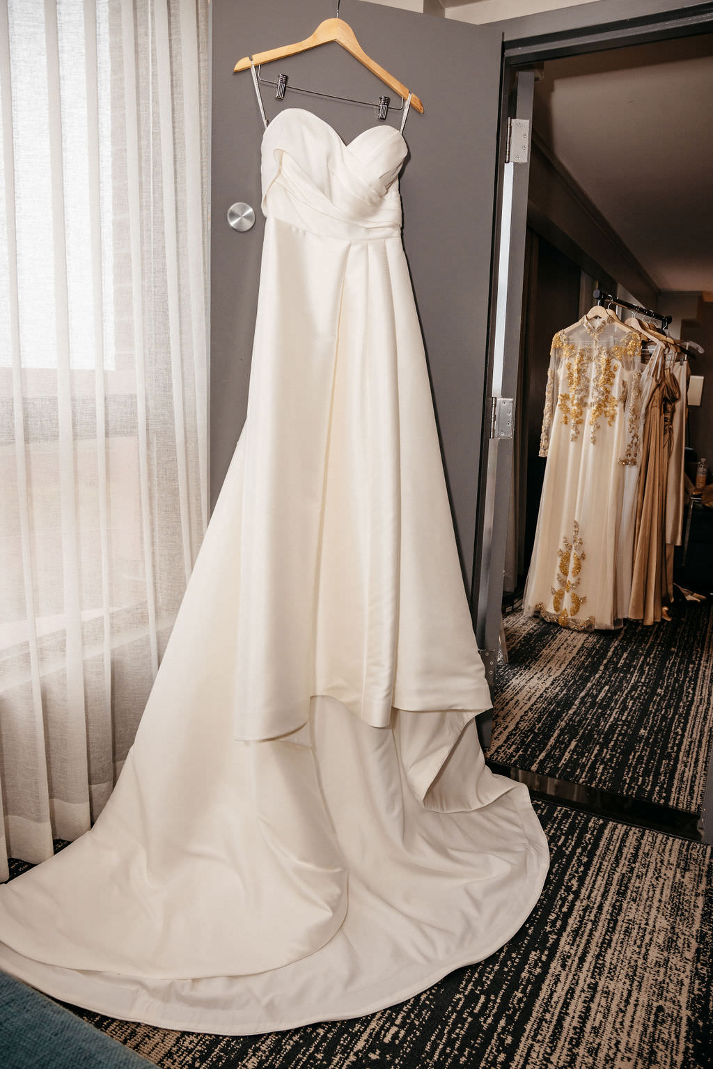 Wedding gown hanging by the window with gold embroidered dresses behind