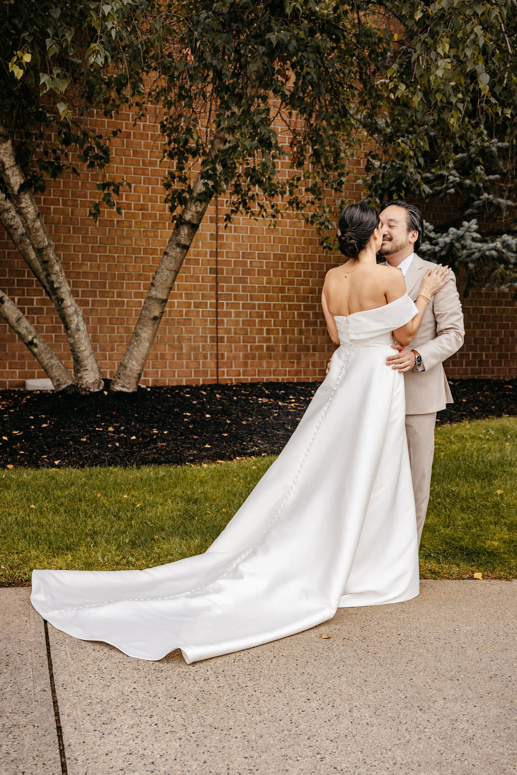 Groom in a tan suit kissing his bride's cheek outside the Boston Marriott