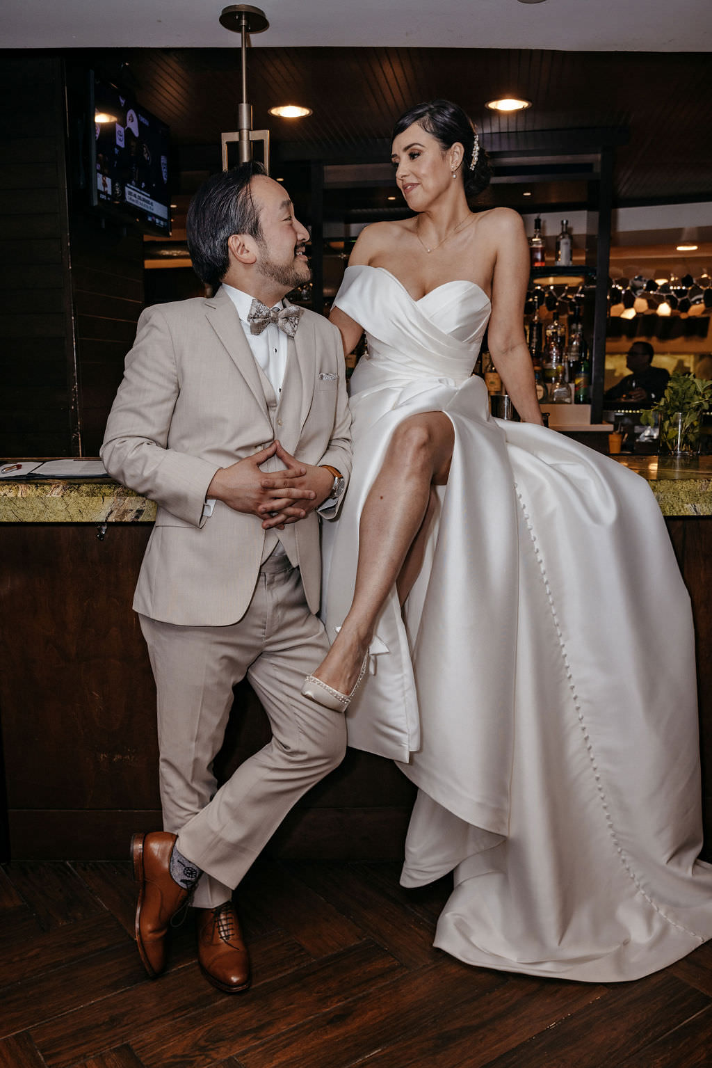 Bride seated on the bar counter laughing with her groom at the hotel bar