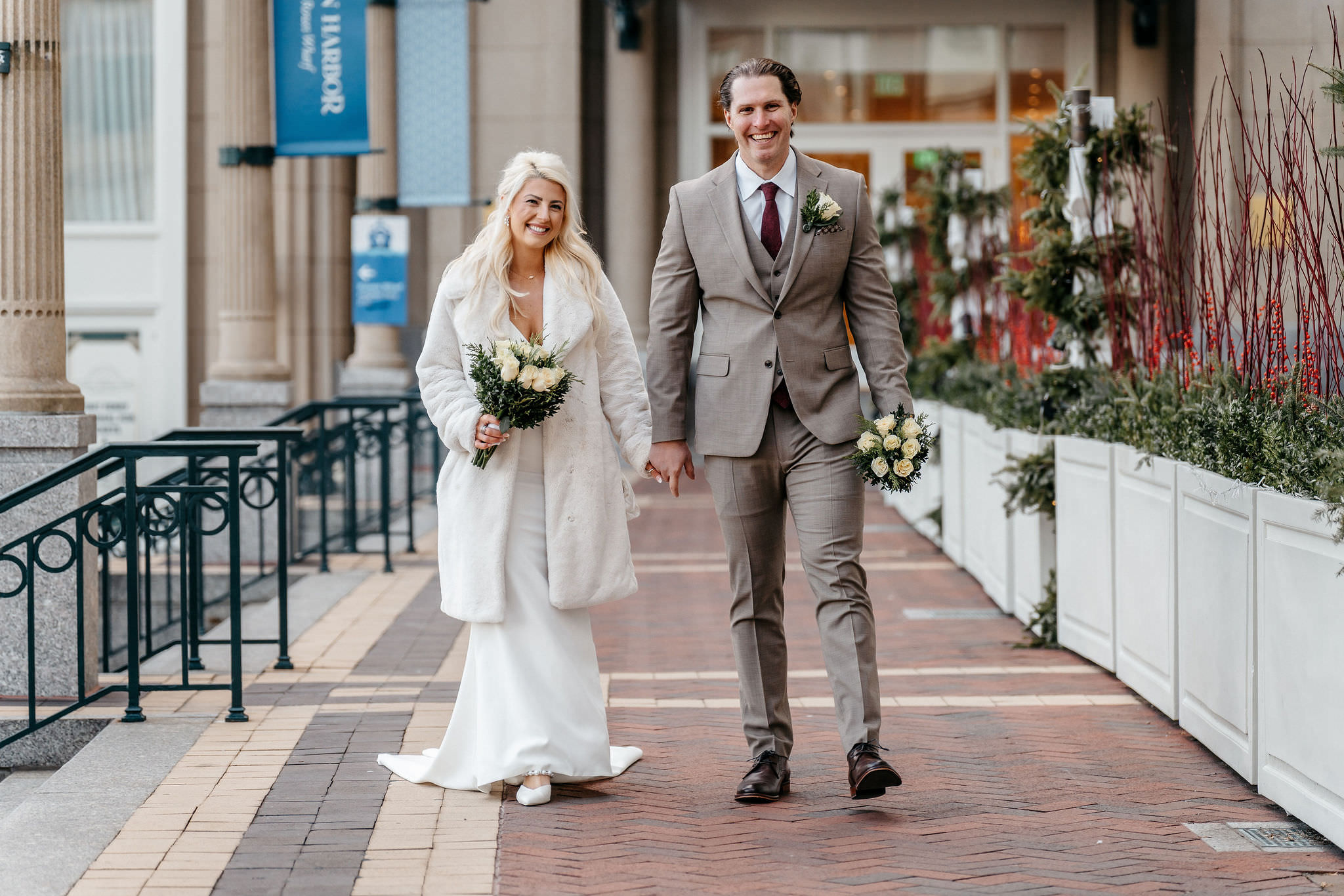 Bride in a fur coat and groom walking hand in hand along the Boston waterfront