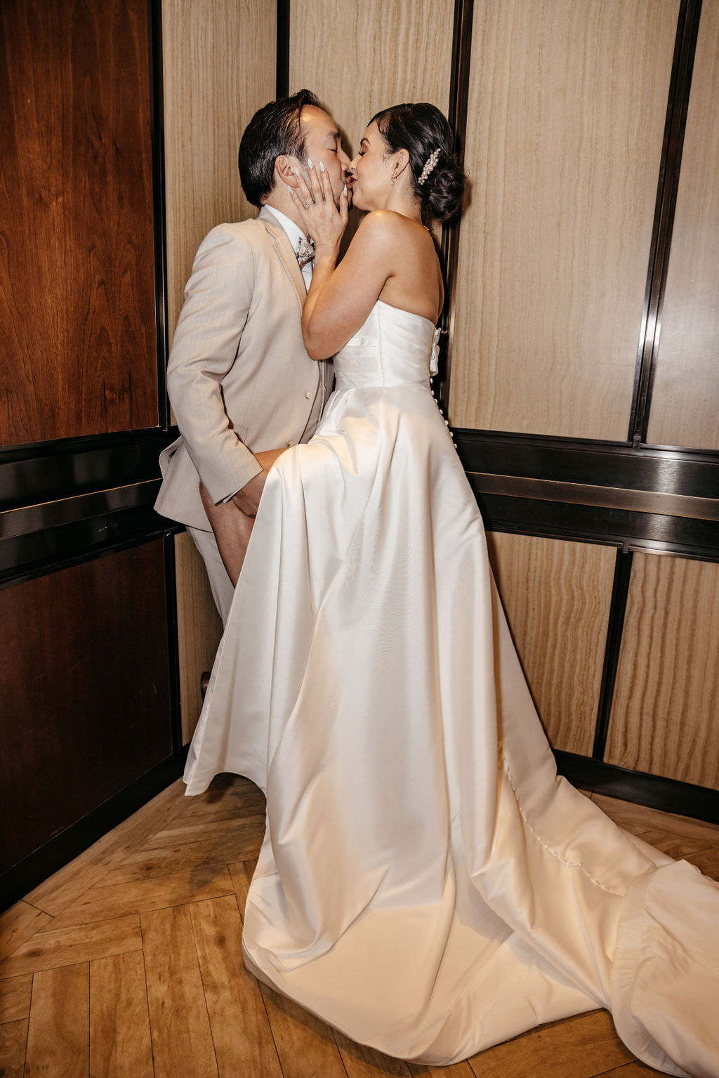 Newlyweds kissing in a wood-paneled elevator, the bride's train filling the floor