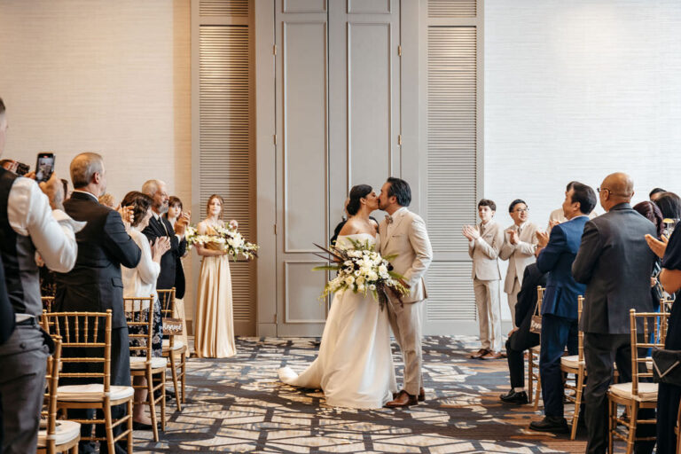 Bride and groom share their first kiss surrounded by guests at their Boston Marriott Burlington wedding.