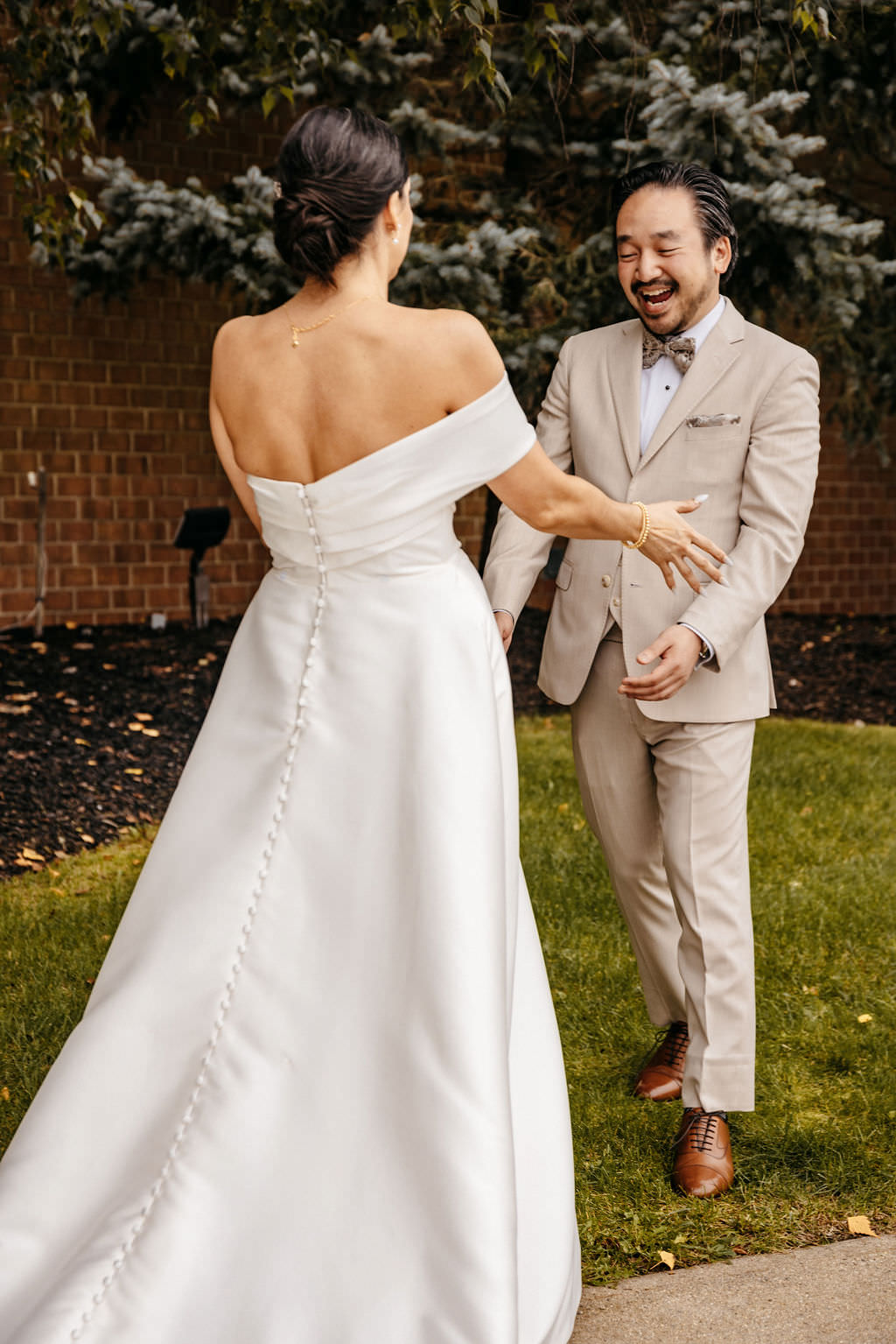 Bride and groom sharing a joyful outdoor first look beside a brick wall