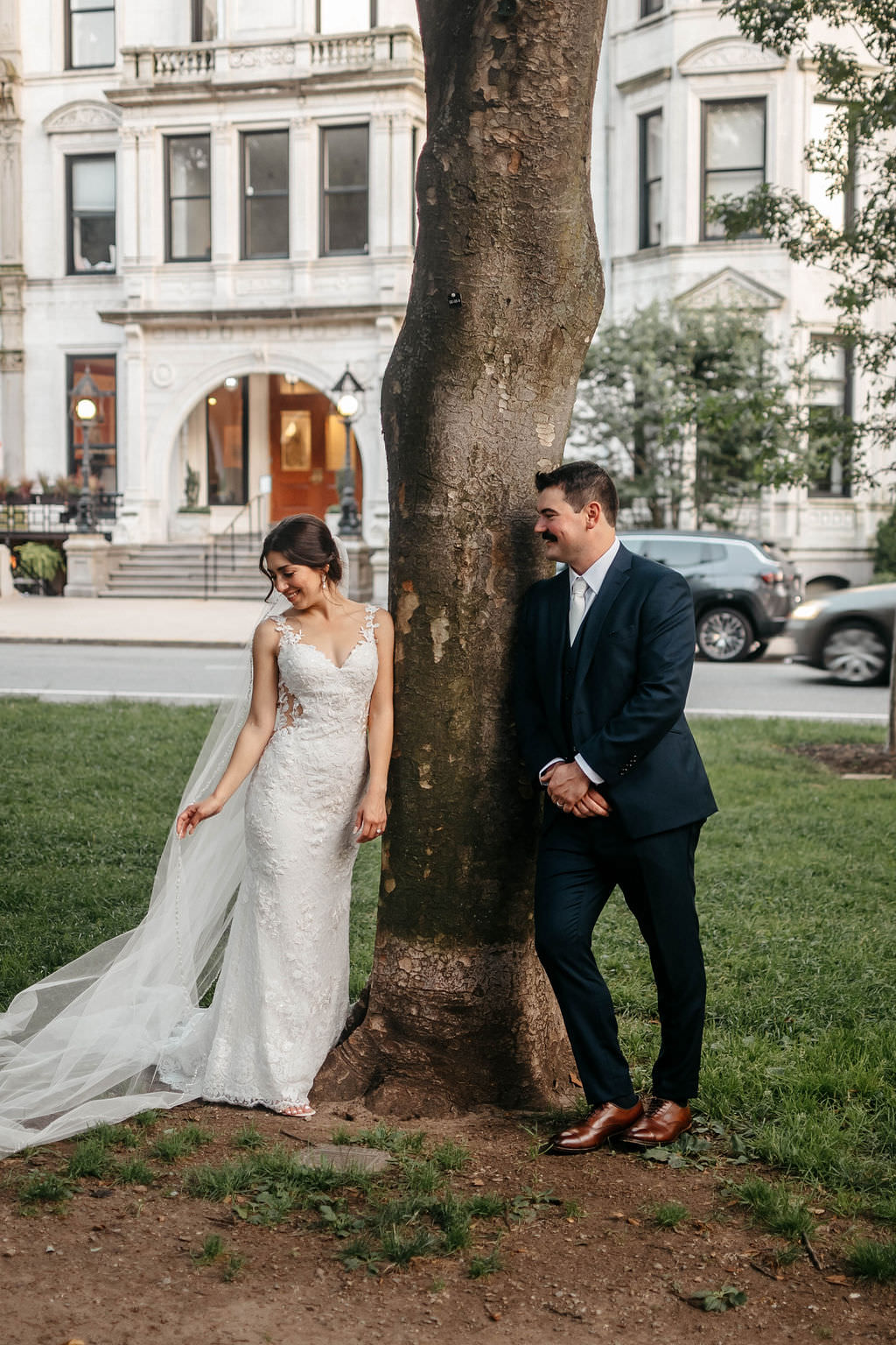 Bride and groom leaning on opposite sides of a tree in a Boston park