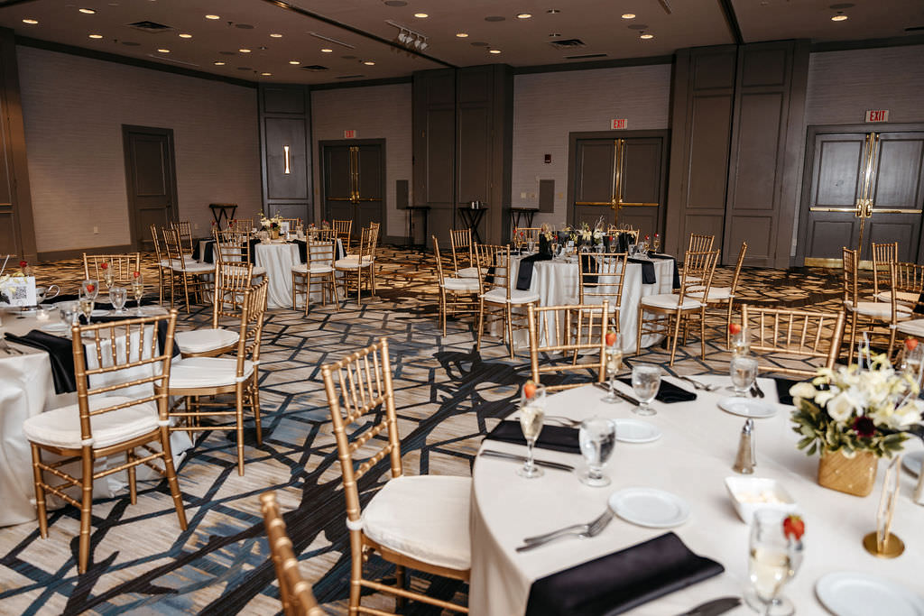 Ballroom reception space with gold chiavari chairs and black napkin settings