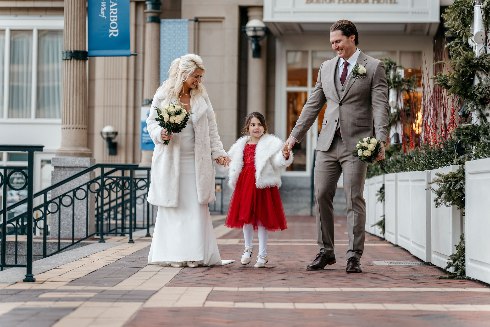 Winter newlyweds walking with their flower girl outside the Boston Harbor Hotel