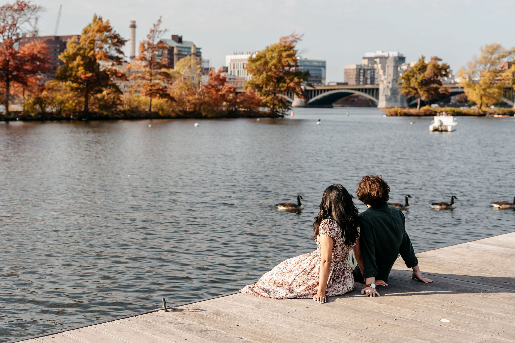 Couple sitting on a Charles River dock with the Longfellow Bridge in fall